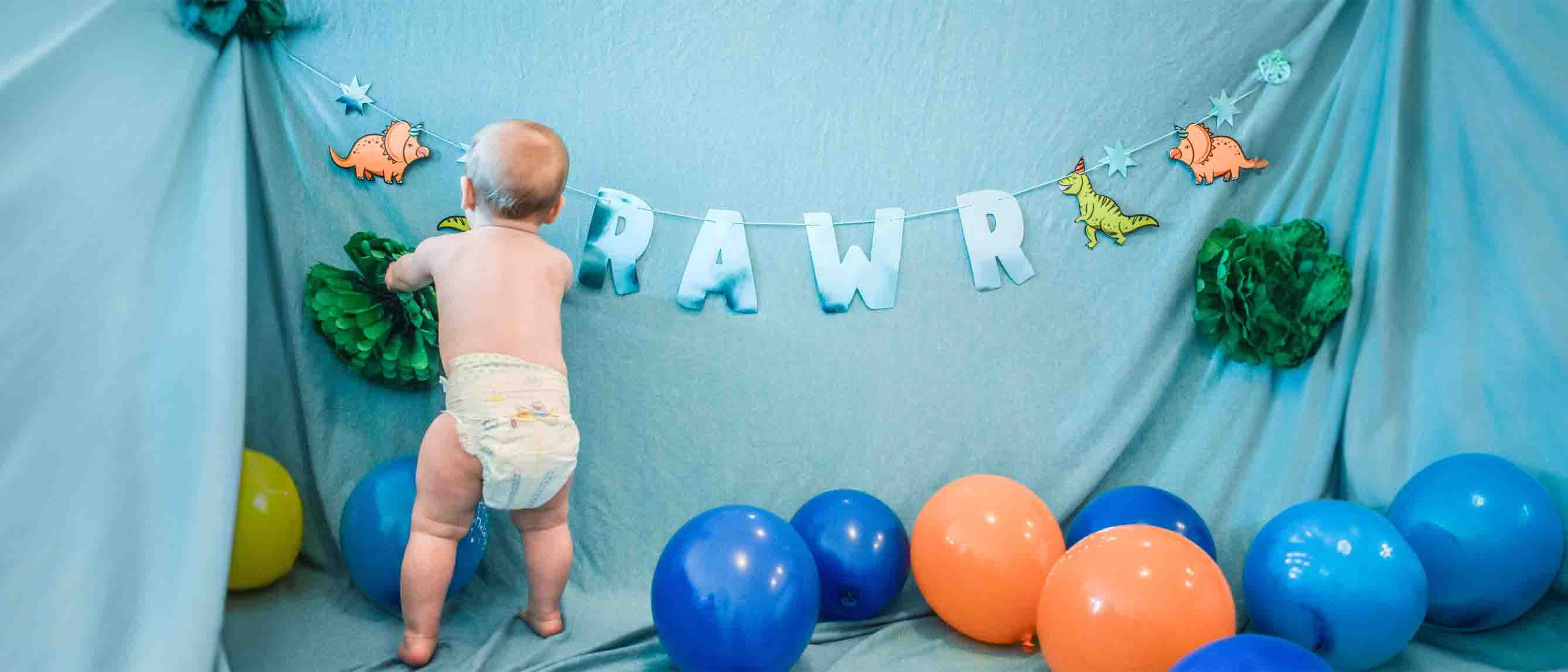 Baby wearing diaper against blue background with balloons