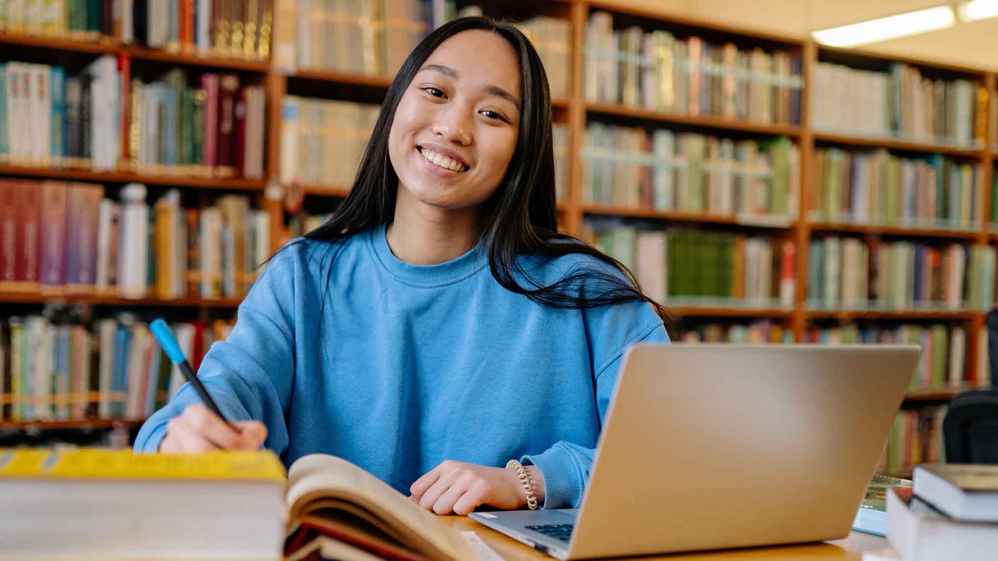 girl in blue sweatshirt smiling while studying at the library 