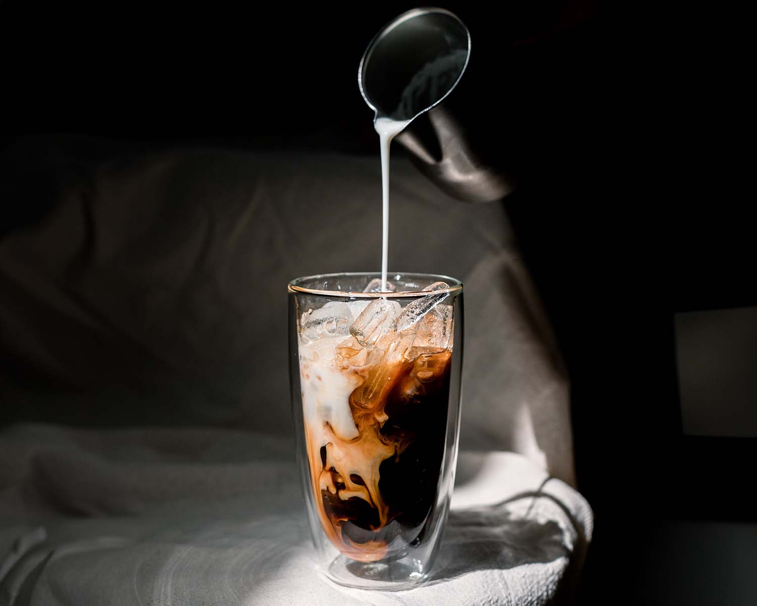 milk being poured over coffee with ice