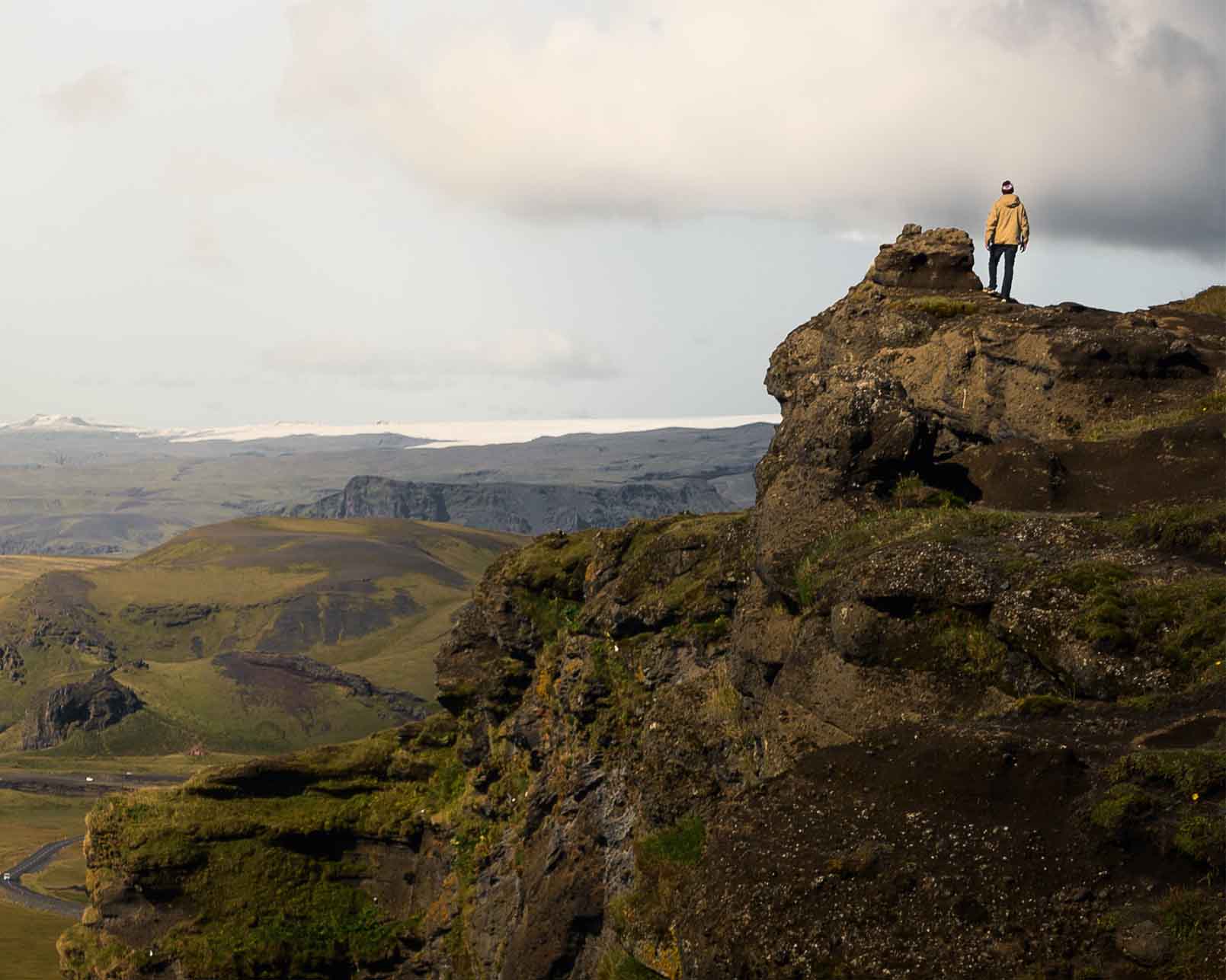 a person in a yellow jacket standing on mountain cliff in Iceland