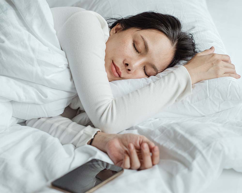 model asleep in bed next to her phone