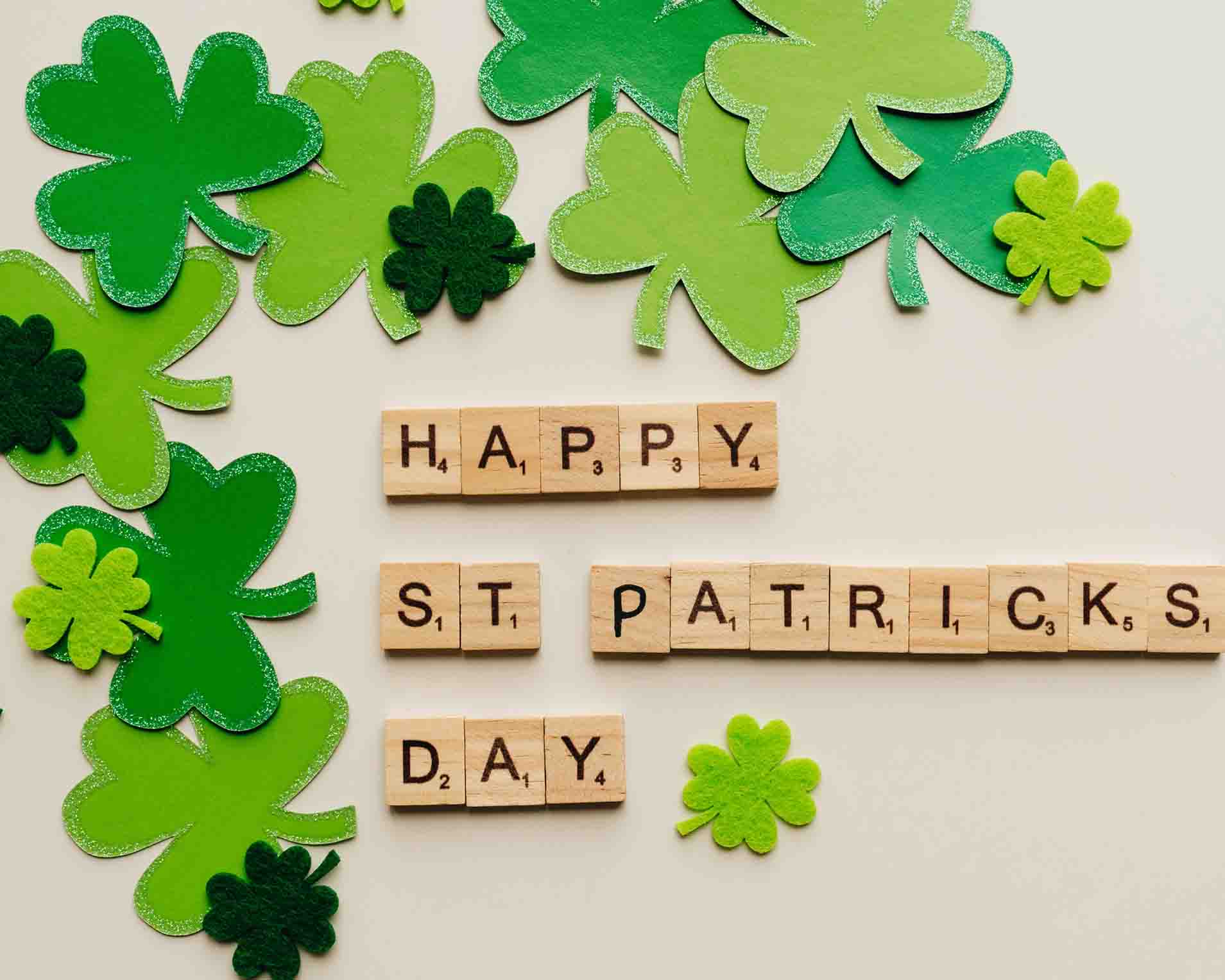 Scrabble letters saying Happy St. Patricks Day and green paper clovers around it