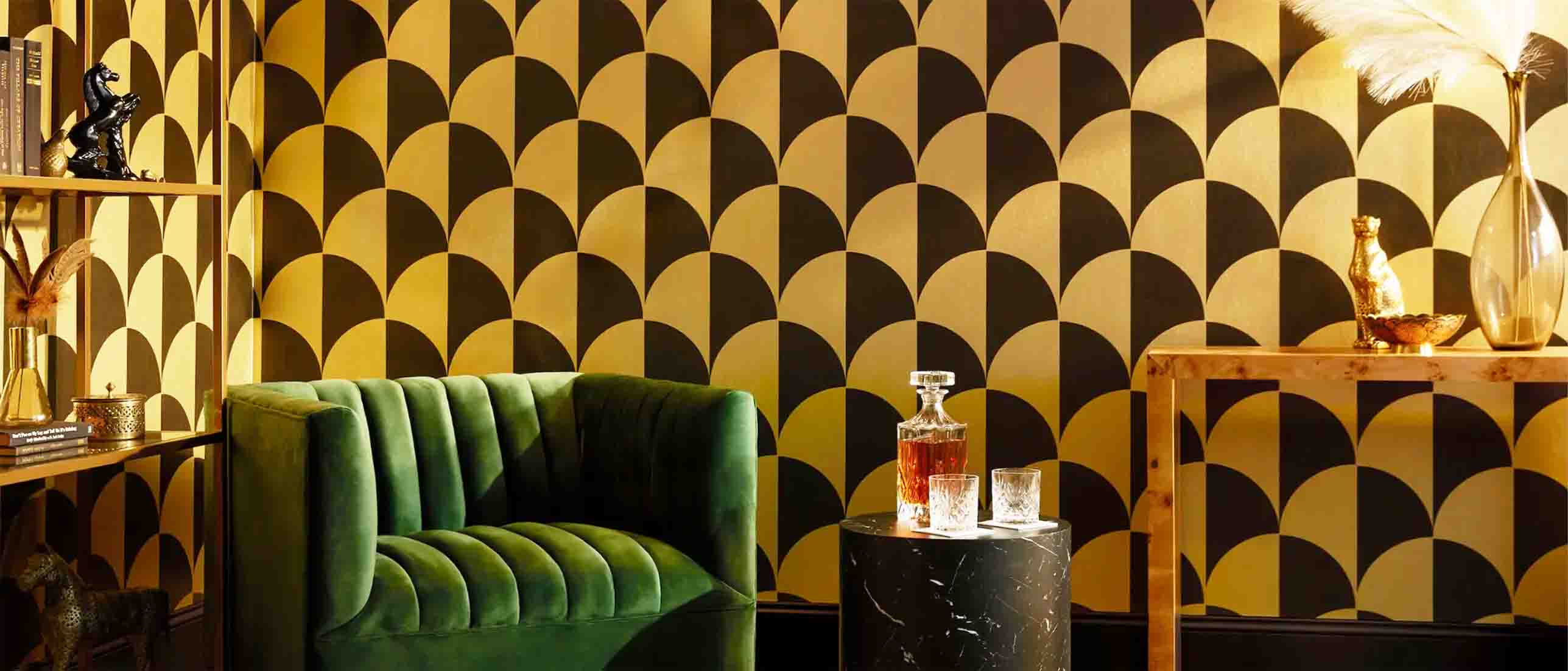 gold metallic round checkers wallpaper, green velvet armchair, bookcase, table and a bottle of drink