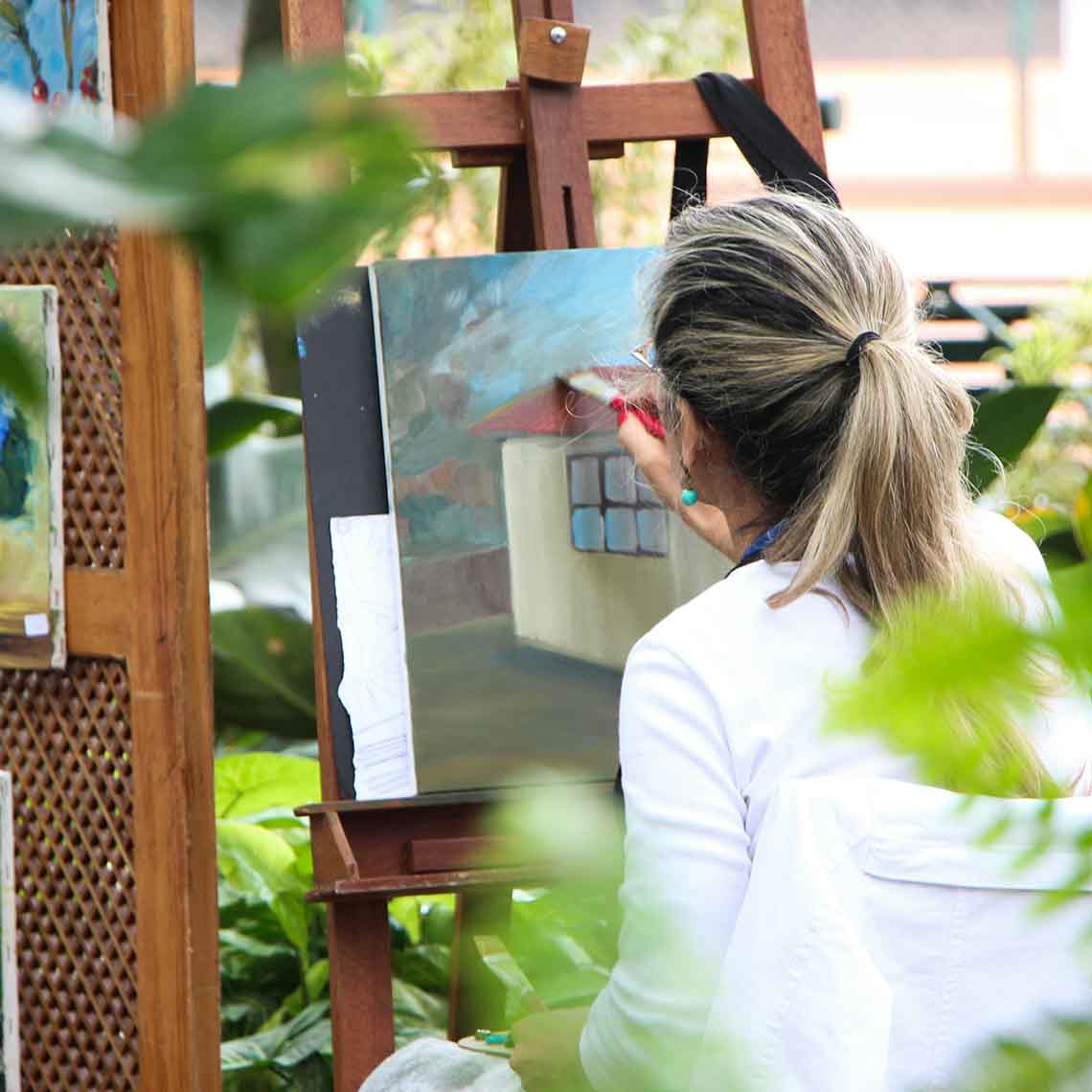 A woman painting a house surrounded by greenery
