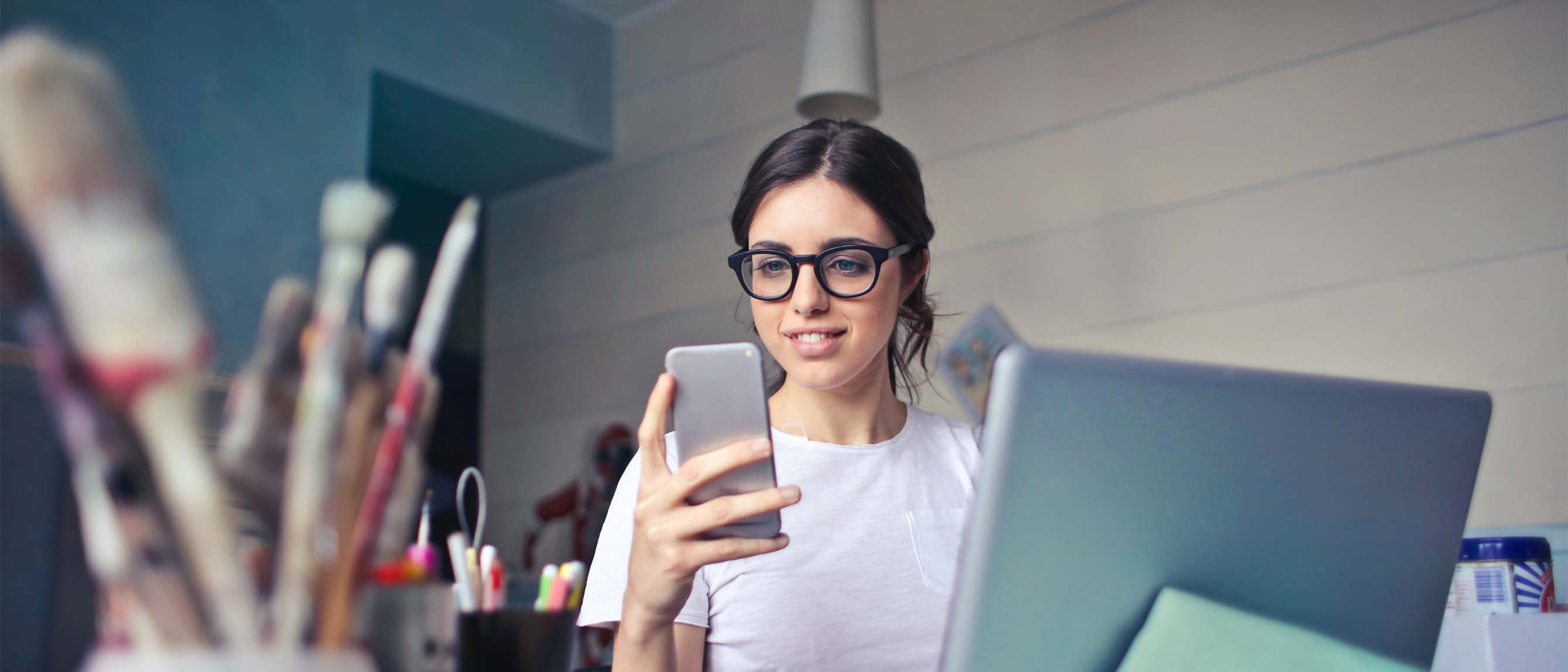 Woman wearing glasses looking at phone and laptop